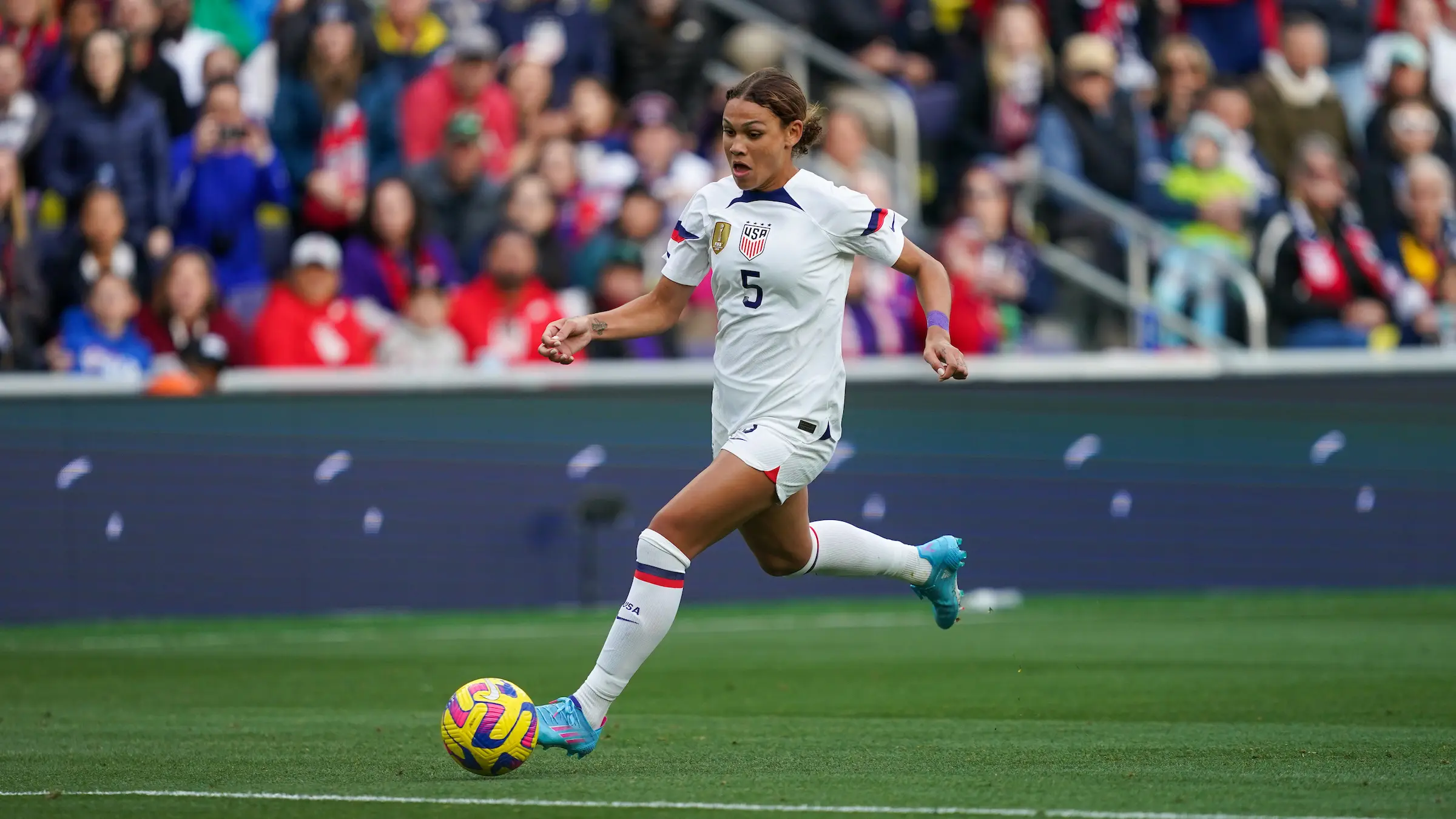 USWNT player in white kit dribbling a soccer ball during a match.